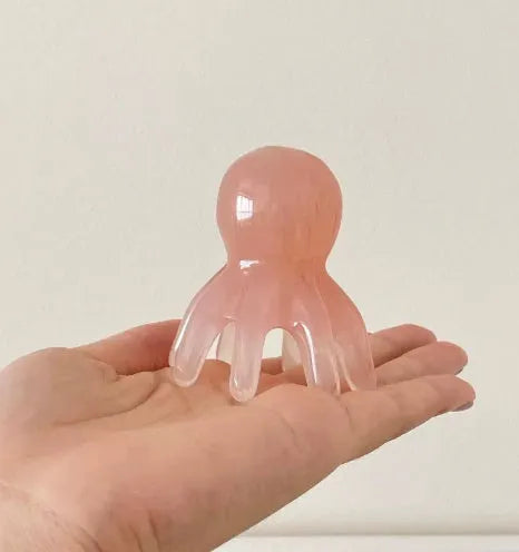 Pink octopus-shaped natural resin massage comb for facial and head massage on a plain background.