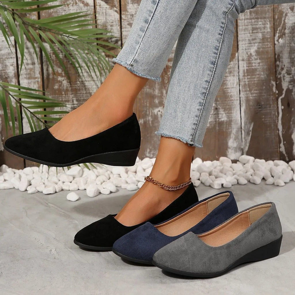 Women's black suede low wedge pumps with pointed toe and shallow mouth design on a rubber sole.