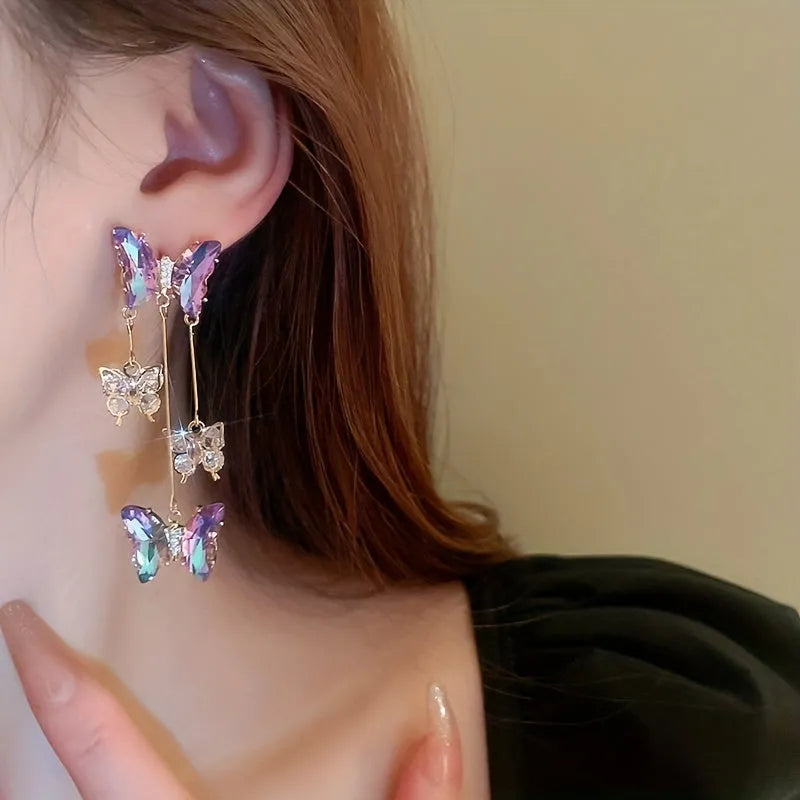 Silver toned earrings with a blue purple butterfly, crystal flowers, and a long tassel drop chain.