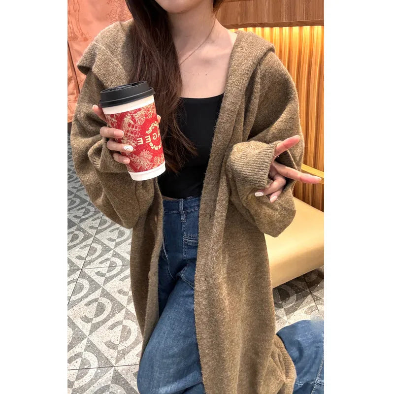 Long grey hooded knitted cardigan on a hanger showing its below-the-knee length and loose fit.