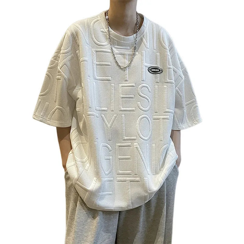 Man wearing a grey loose-fit T-shirt with a retro-style 3D raised letter print across the chest.