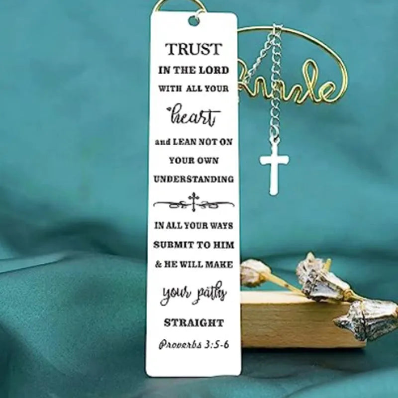 A polished stainless steel bookmark with an engraved inspirational verse, shown against an open book.