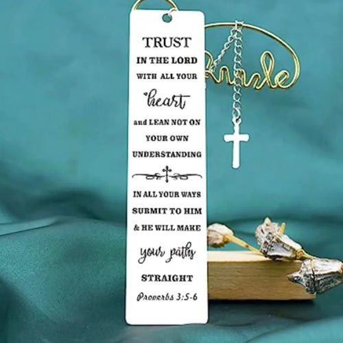 A polished stainless steel bookmark with an engraved inspirational verse, shown against an open book.