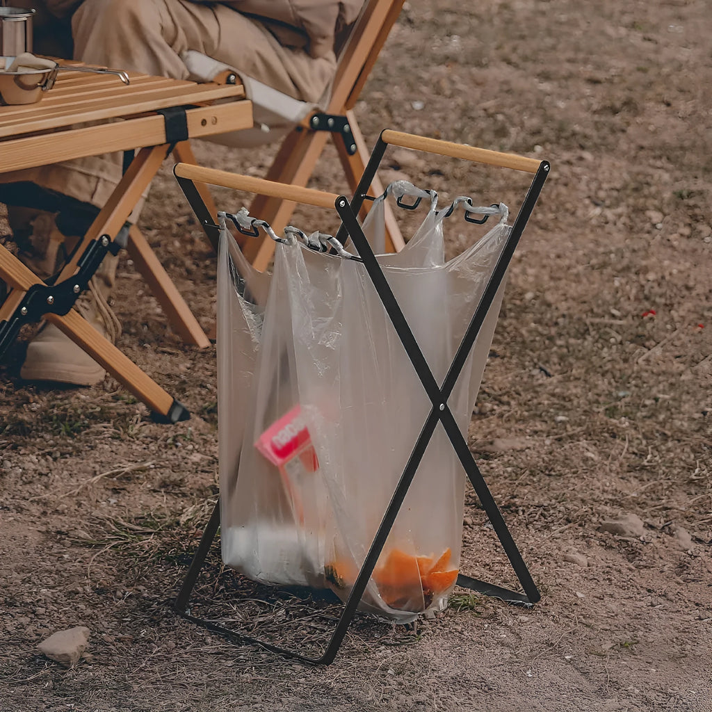 Black folding outdoor trash rack with a wooden handle, holding a rubbish sack.