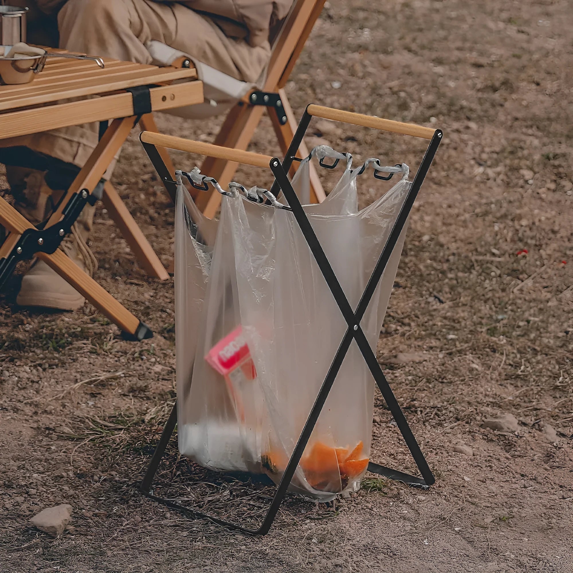 Black folding outdoor trash rack with a wooden handle, holding a rubbish sack.