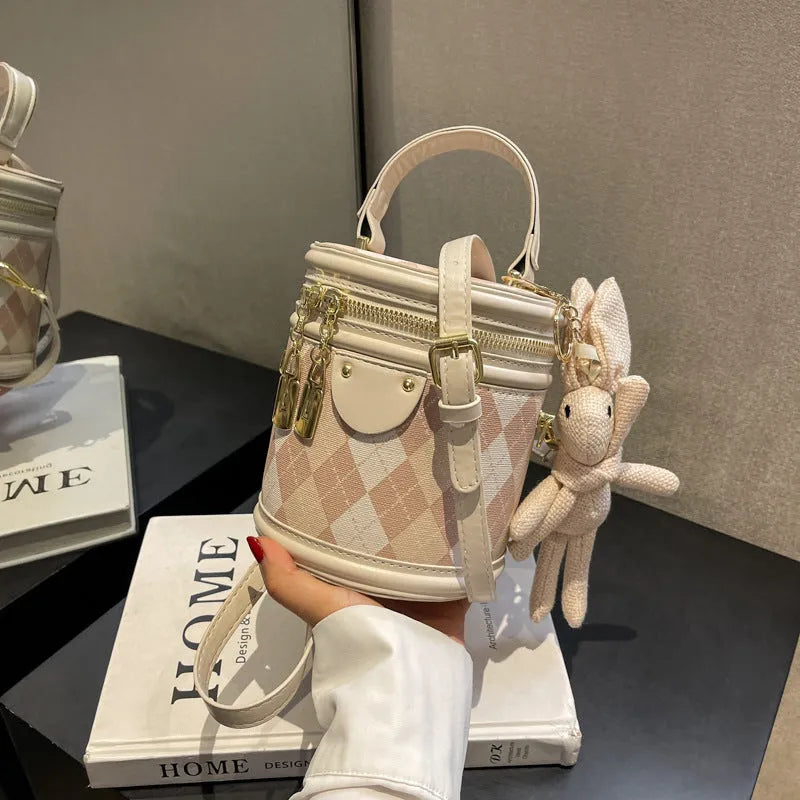Textured rhombus cylindrical PU bucket bag in beige with white rabbit pendant, 14 cm wide.