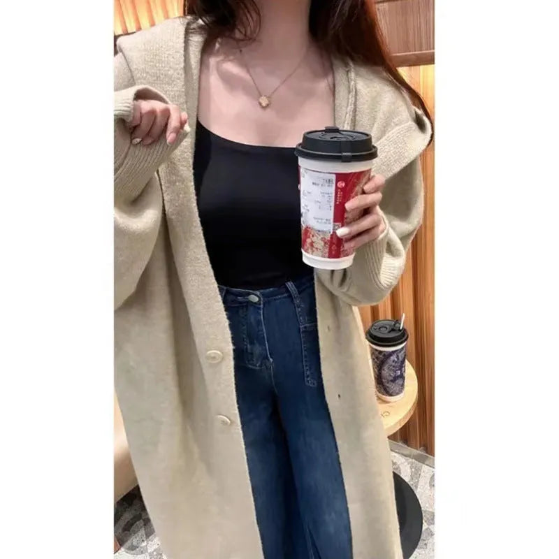 Long grey hooded knitted cardigan on a hanger showing its below-the-knee length and loose fit.
