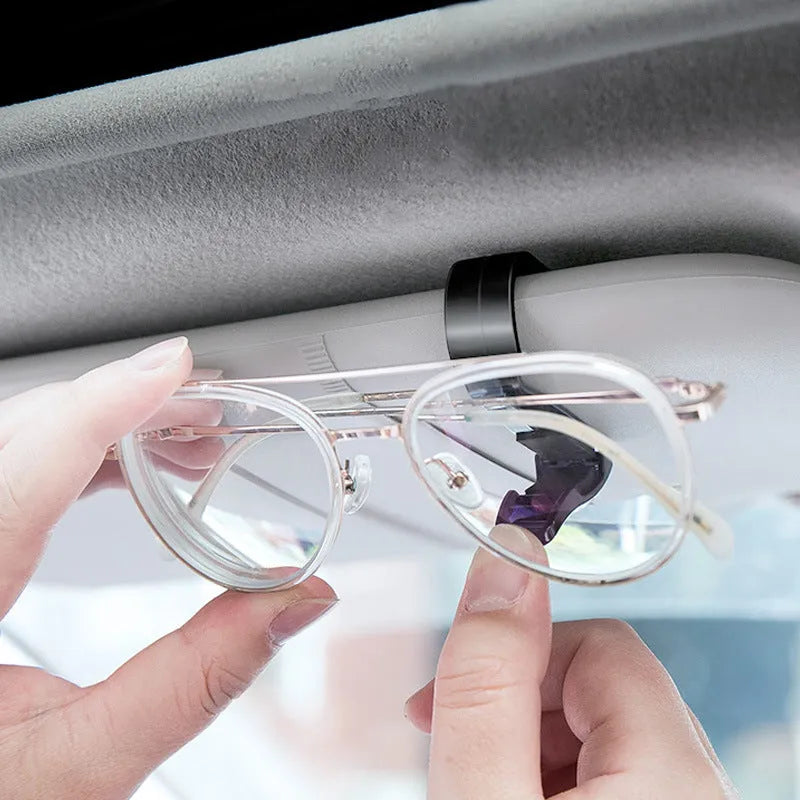 Black plastic multifunctional clip for mounting on a car sunshade to hold glasses, tickets, and ID cards.