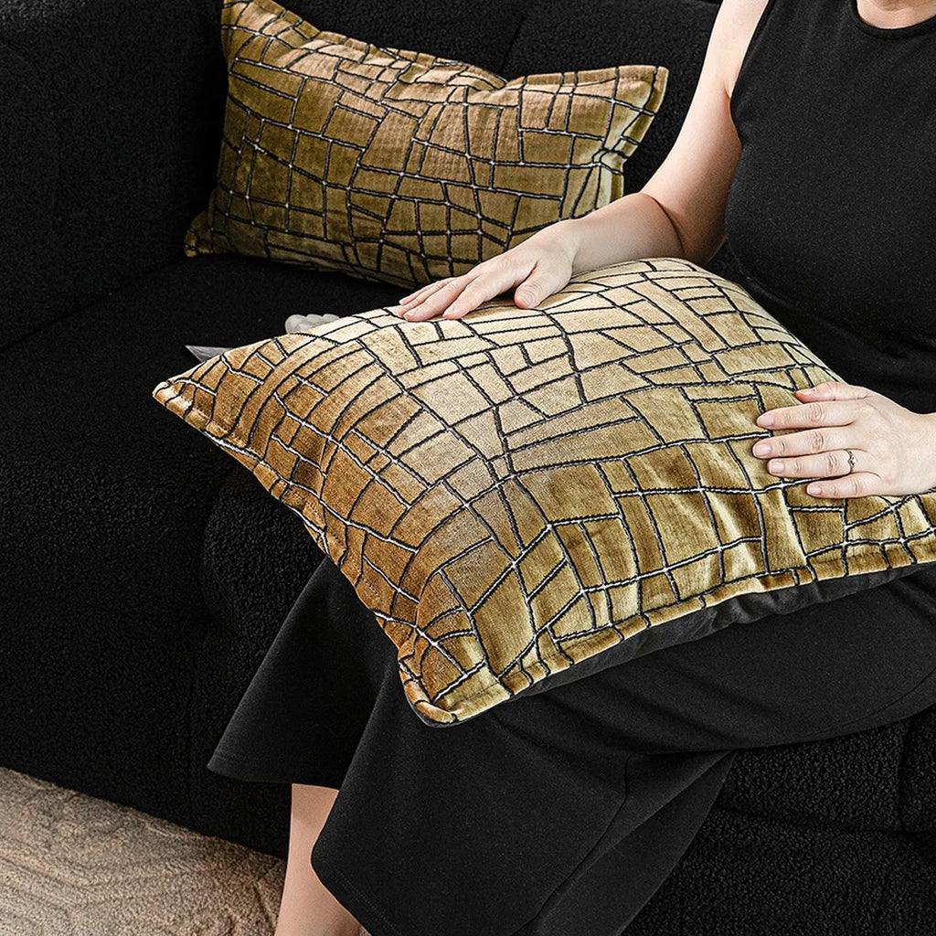 Gold geometric pattern on a velvet square cushion and a rectangular waist pillow against a sofa.