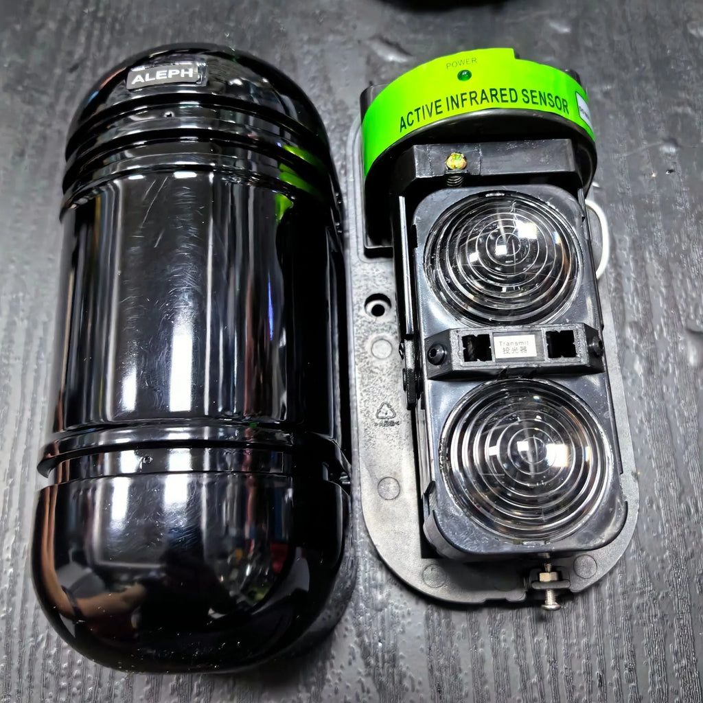 A pair of black wall-mounted infrared security detectors with wired terminals.