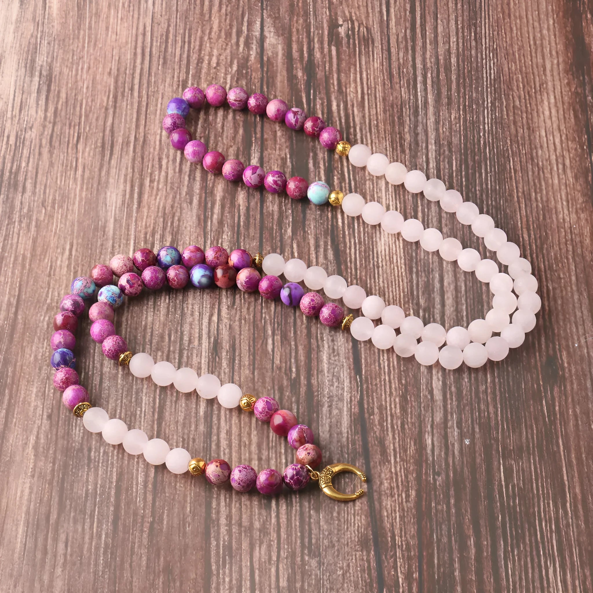 Round pink Emperor Stone pendant on a silver-tone chain, laid flat.