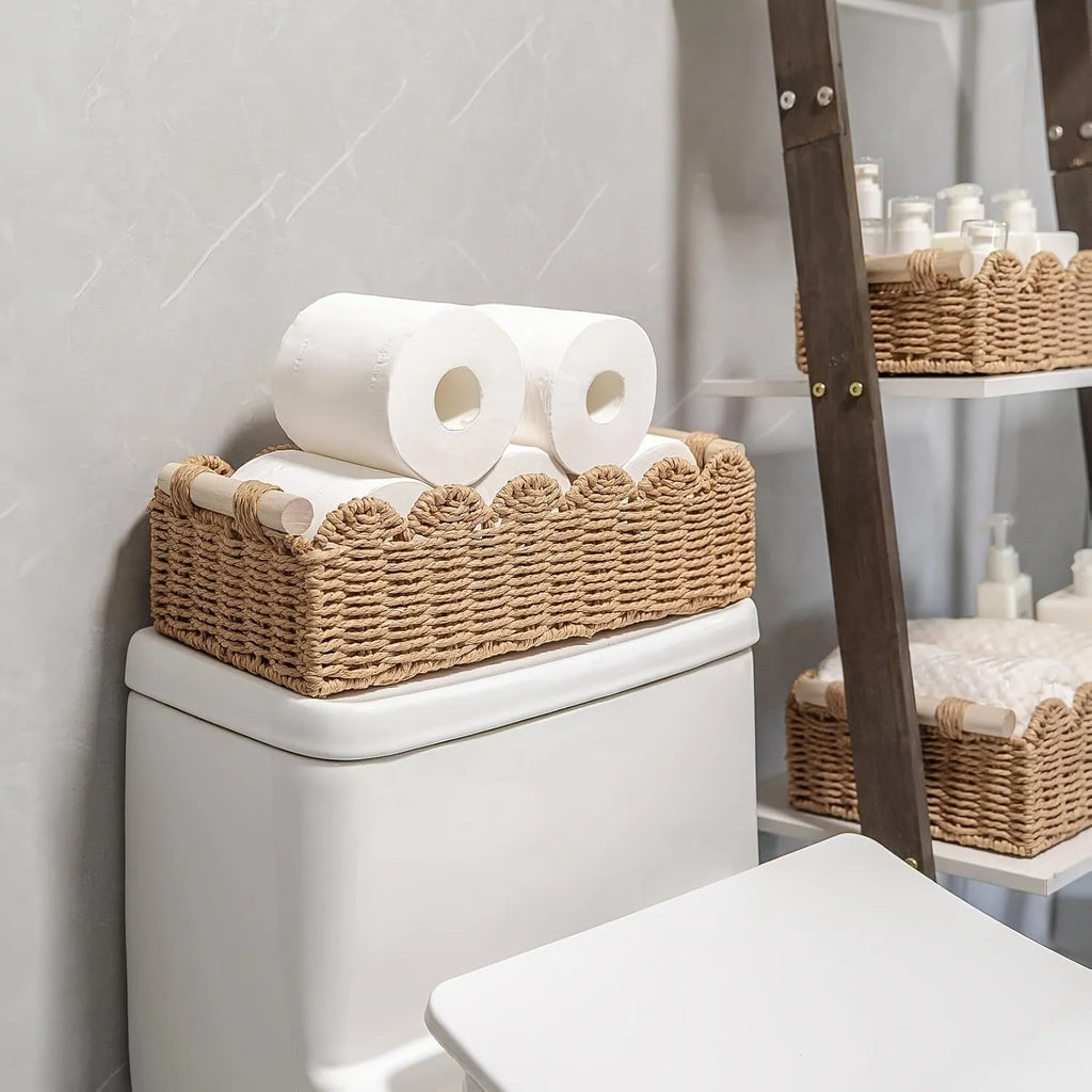 Modern woven paper storage basket in khaki colour on a wooden desktop, holding remote controls and pens.