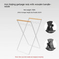 Black folding outdoor trash rack with a wooden handle, holding a rubbish sack.