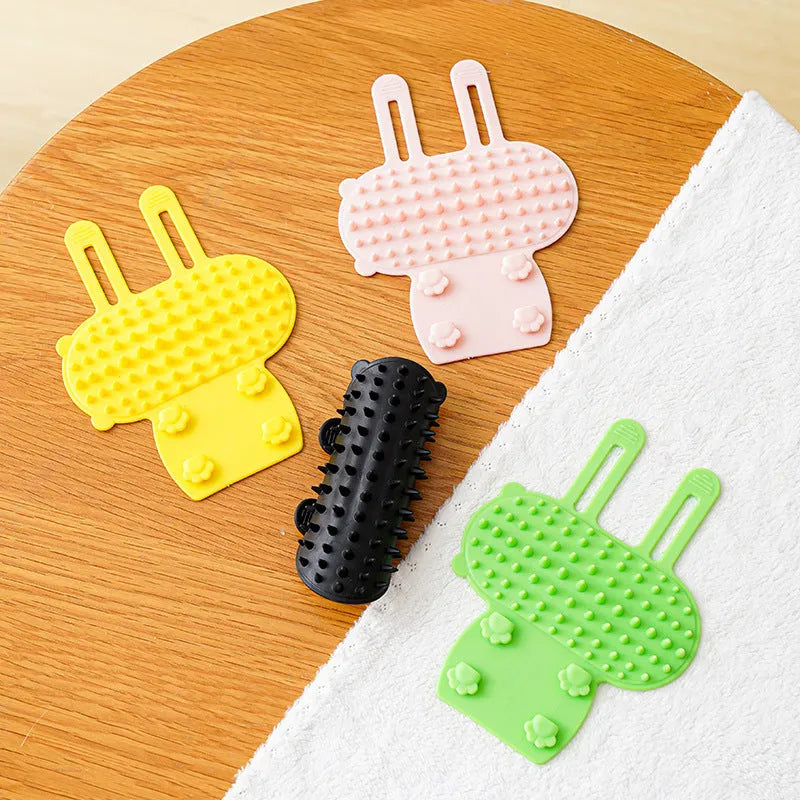 Silicone cat grooming comb with adjustable strap mounted on a table leg, shown in green colour.