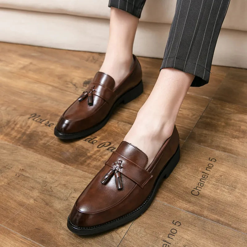 Men's black slip-on loafer with tassel detail and rubber sole on white background
