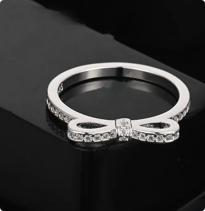 Silver-coloured bow-shaped ring with sparkling zircon crystal stones on a finger.