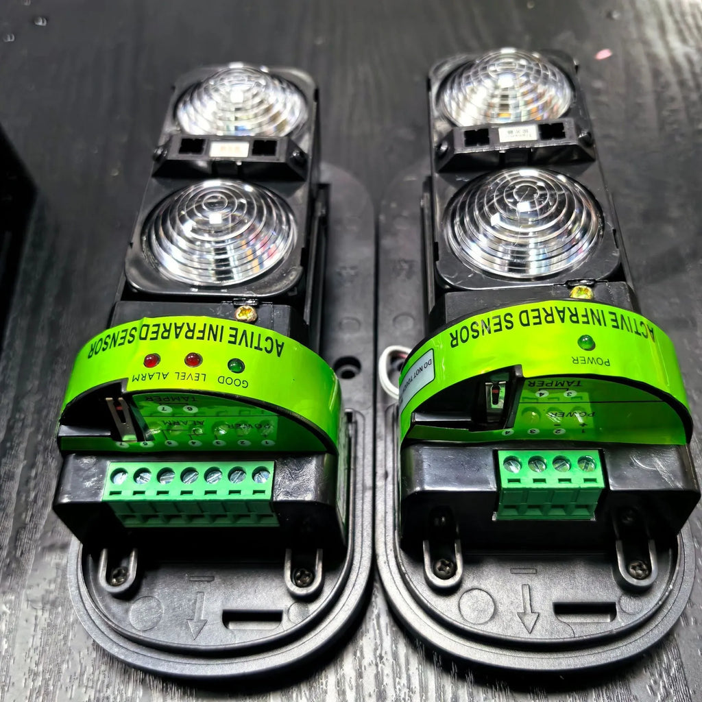 A pair of black wall-mounted infrared security detectors with wired terminals.