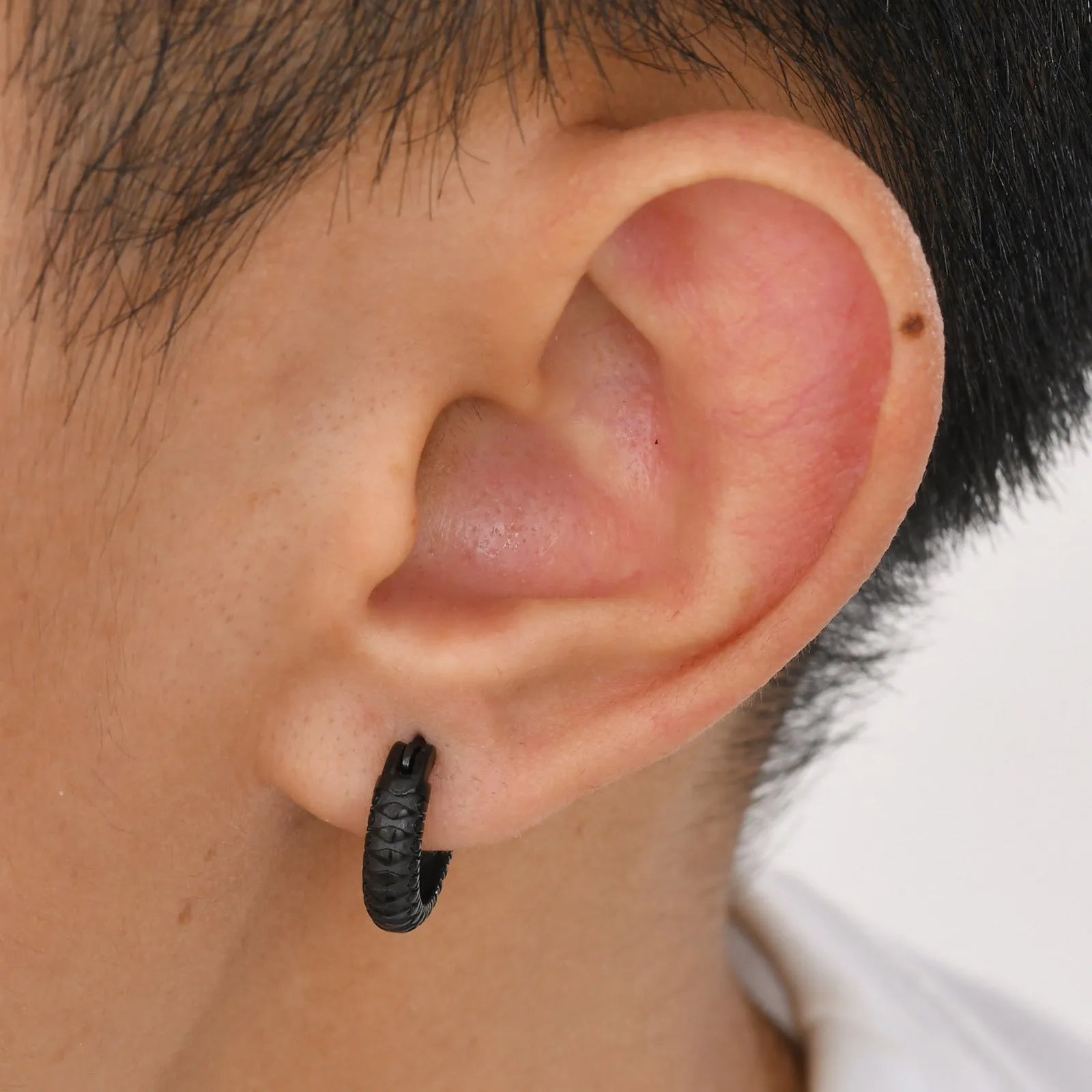 A pair of stainless steel earrings with a raised snake pattern texture in a black or gold finish.