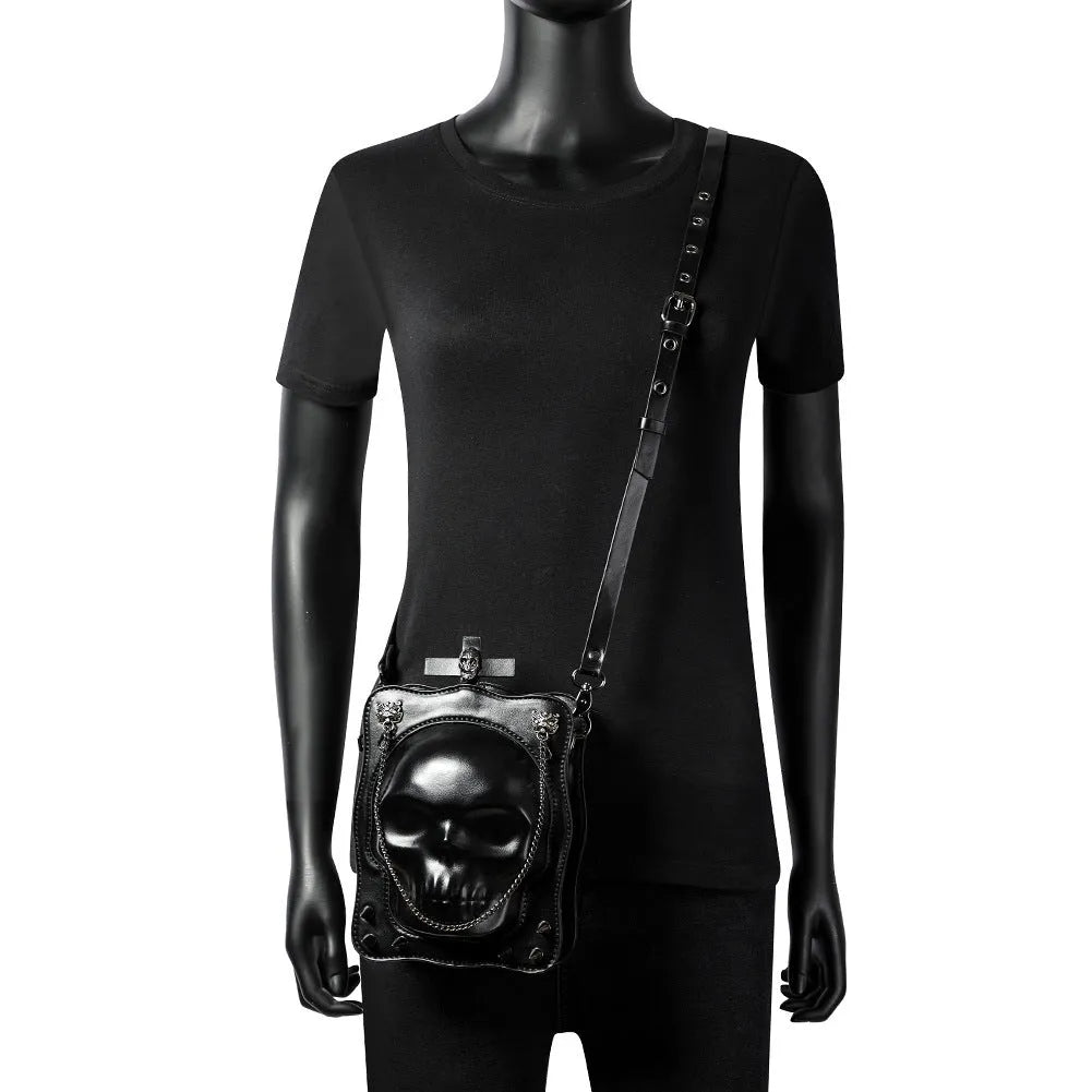 Black mini square crossbody bag with skull embossing, chain detail, and metal rivets on a vertical PU leather messenger bag.