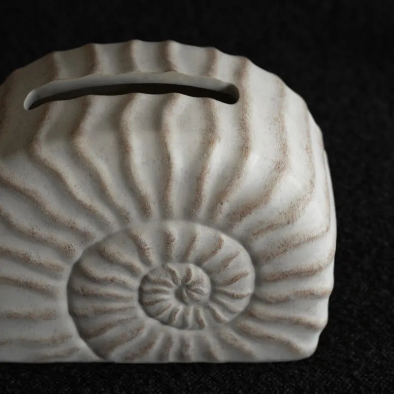 Solid resin conch-shaped tissue box cover in a natural colour on a table.