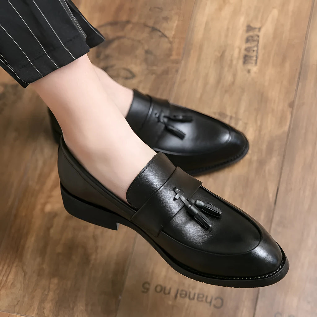 Men's black slip-on loafer with tassel detail and rubber sole on white background