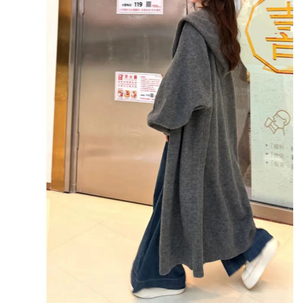 Long grey hooded knitted cardigan on a hanger showing its below-the-knee length and loose fit.