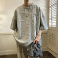Man wearing a grey loose-fit T-shirt with a retro-style 3D raised letter print across the chest.