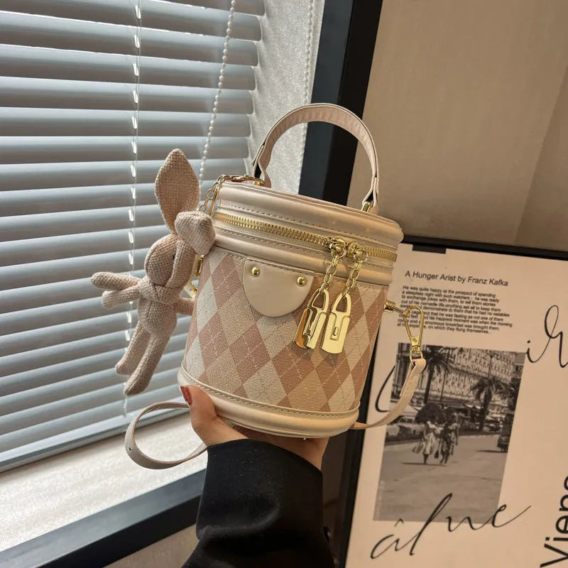 Textured rhombus cylindrical PU bucket bag in beige with white rabbit pendant, 14 cm wide.