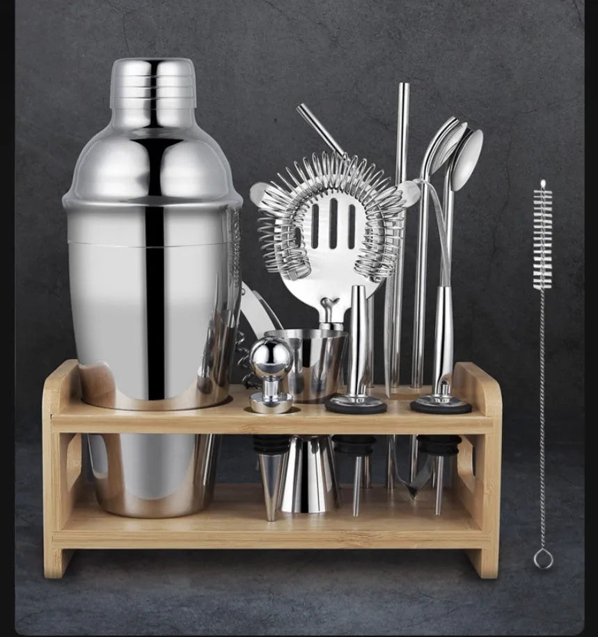 23-piece stainless steel cocktail set with shaker, jigger, strainer, and other bar tools on a wooden surface.