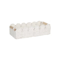 Modern woven paper storage basket in khaki colour on a wooden desktop, holding remote controls and pens.