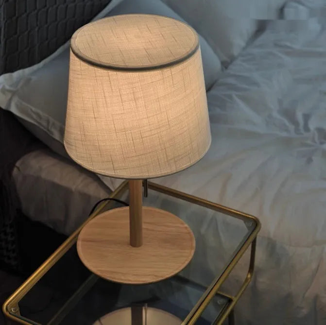 Walnut coloured solid wood table lamp with white cloth lampshade and black cable switch.