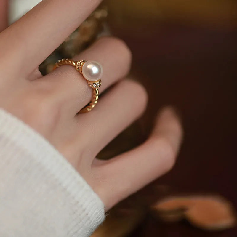 Adjustable geometric twist copper ring with a central pearl, shown in gold and silver colour options.