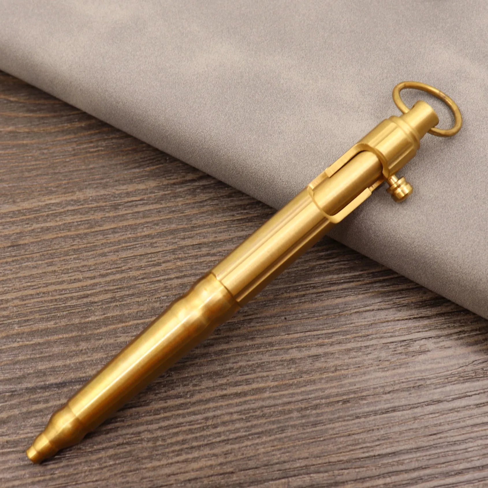 Brass bolt-action tactical pen in a retro copper finish, showing press mechanism and textured barrel.