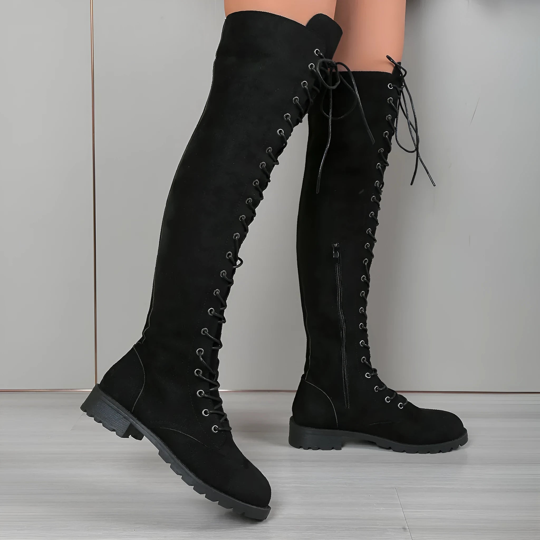 Black lace-up over-the-knee boots with a flat rubber sole and decorative stitching on the faux leather upper