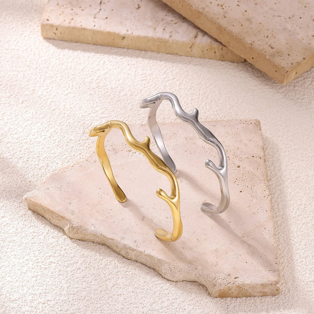 Simple irregular stainless steel gold-plated bracelet in silver finish on plain background