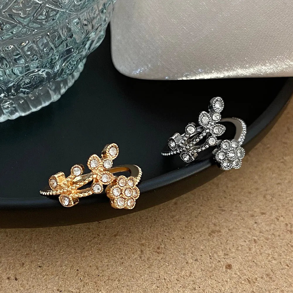 Women's open ring made of copper with a diamond finish, shaped as a detailed flower with leaves, shown in gold and white colour options.