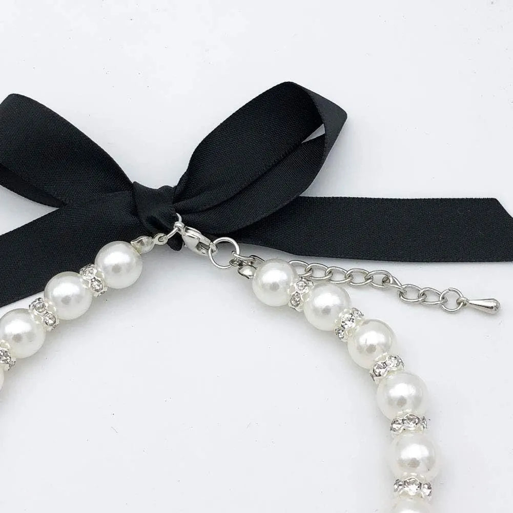 Adjustable blue pearl and rhinestone dog necklace collar with ribbon bow on a small dog.