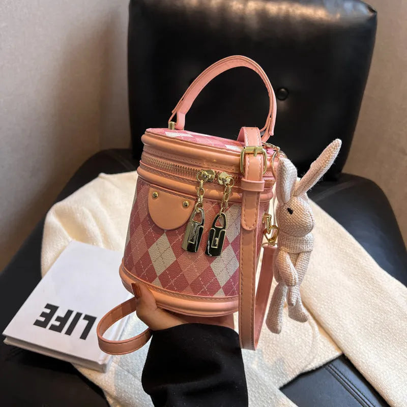 Textured rhombus cylindrical PU bucket bag in beige with white rabbit pendant, 14 cm wide.