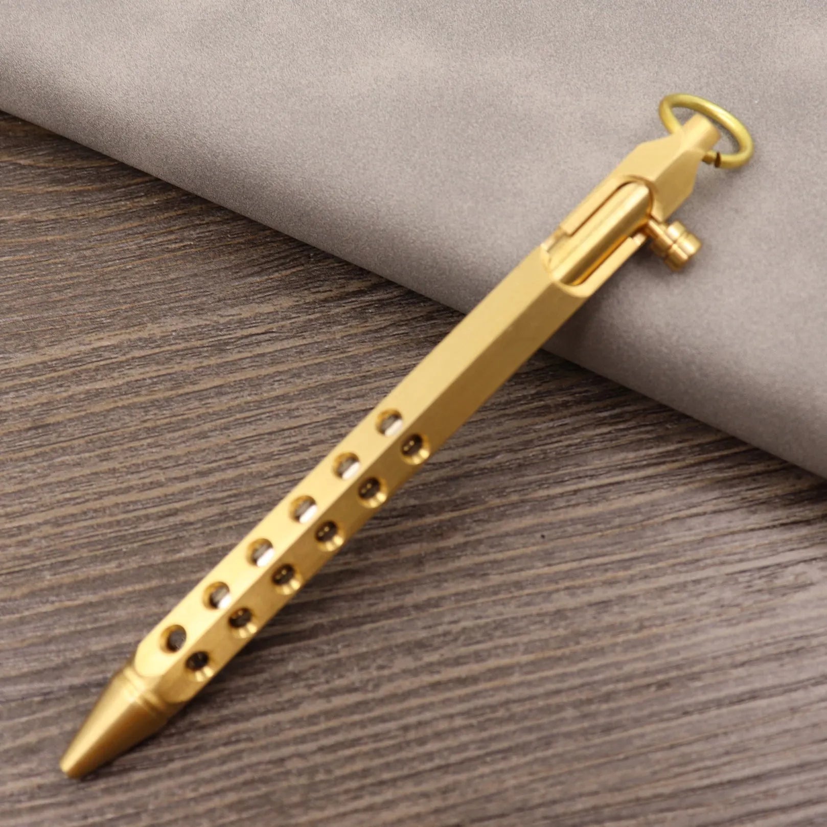 Brass bolt-action tactical pen in a retro copper finish, showing press mechanism and textured barrel.