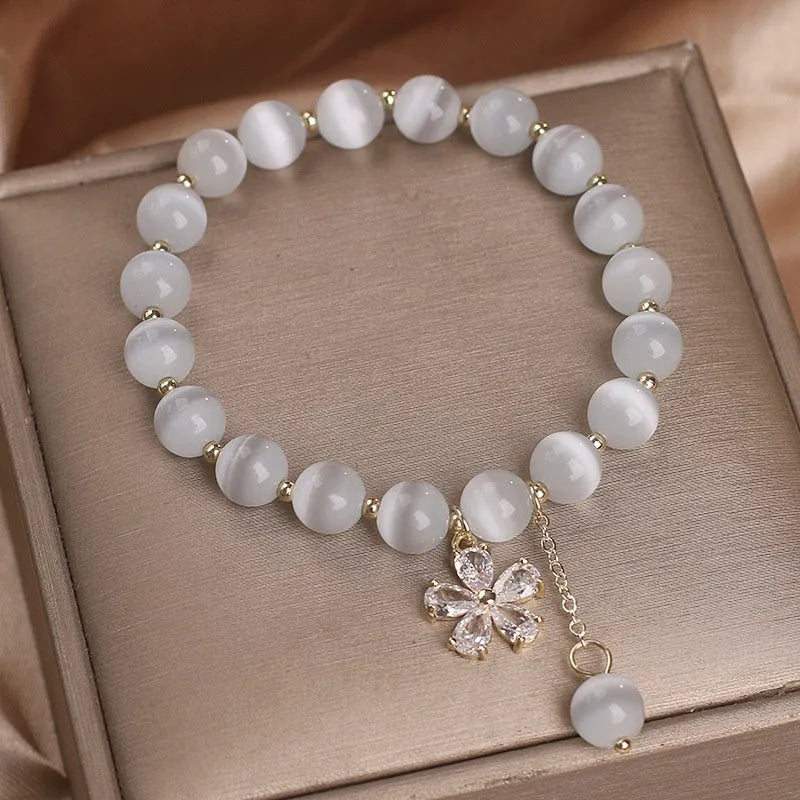 Women's white cat's eye bracelet with flower tassel and safety buckle pendant on wrist