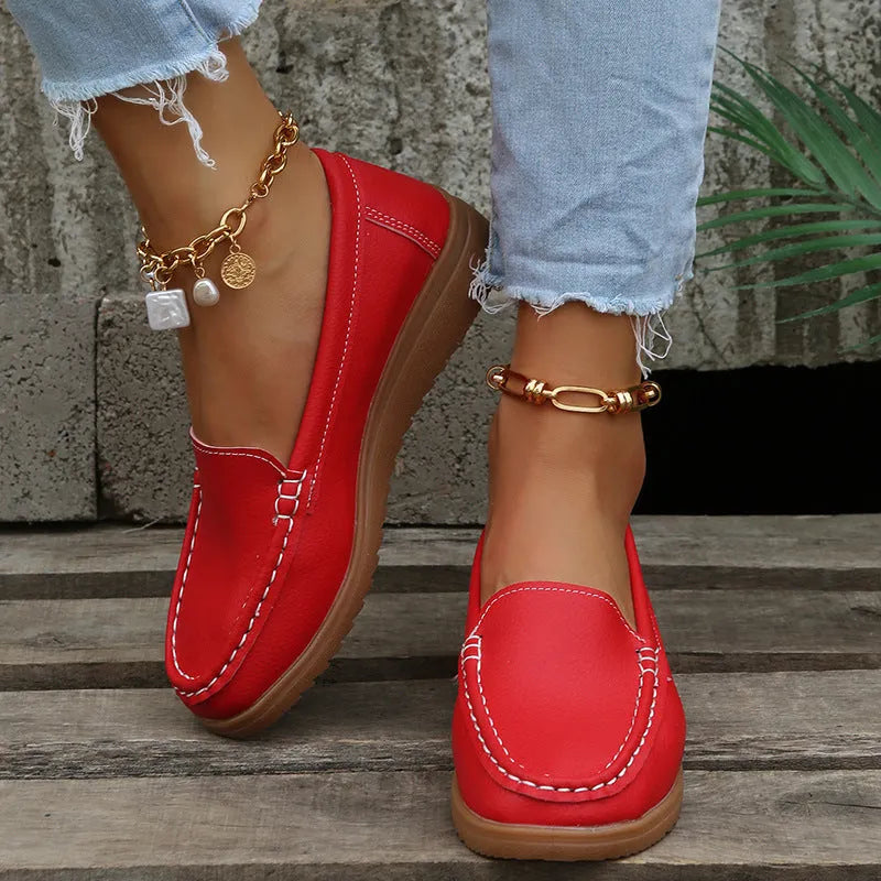 Women's flat slip-on loafers in PU leather with car stitch detail and a round toe, shown on a white background.