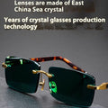 Dark green frameless crystal sunglasses with case and cleaning cloth on a solid background.