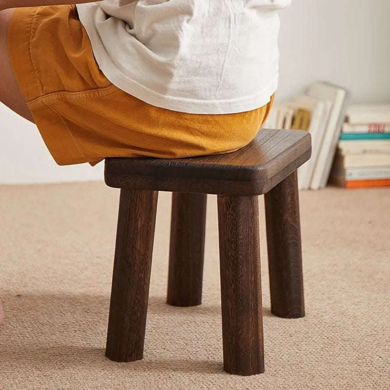 Solid wood distressed finish shoe changing stool with bracket legs in a living room setting.