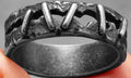Close-up of a stainless steel double ring with punk stitching style detail on a dark background.