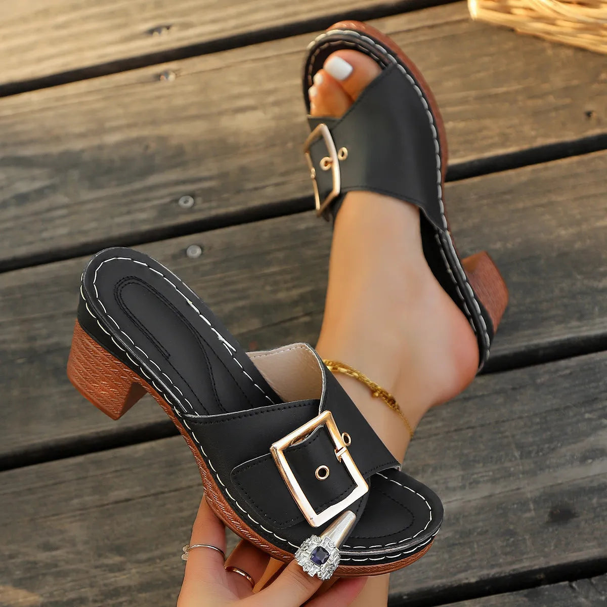 Women's black chunky heel slippers with a large silver metal buckle strap on a rubber sole.