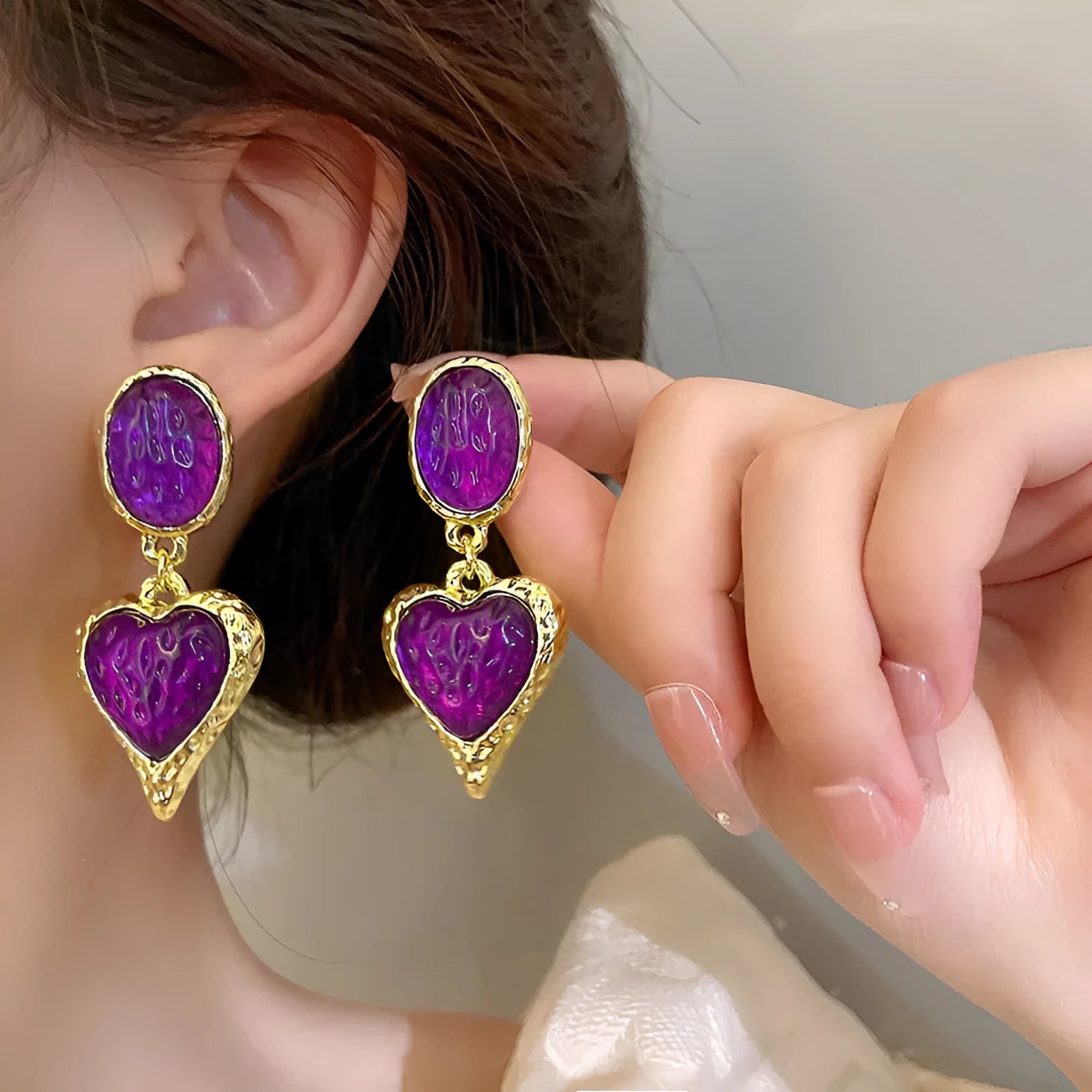 A pair of alloy silver needle pleated oval love heart stud earrings on a purple background.