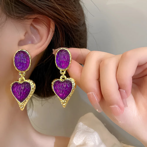 A pair of alloy silver needle pleated oval love heart stud earrings on a purple background.