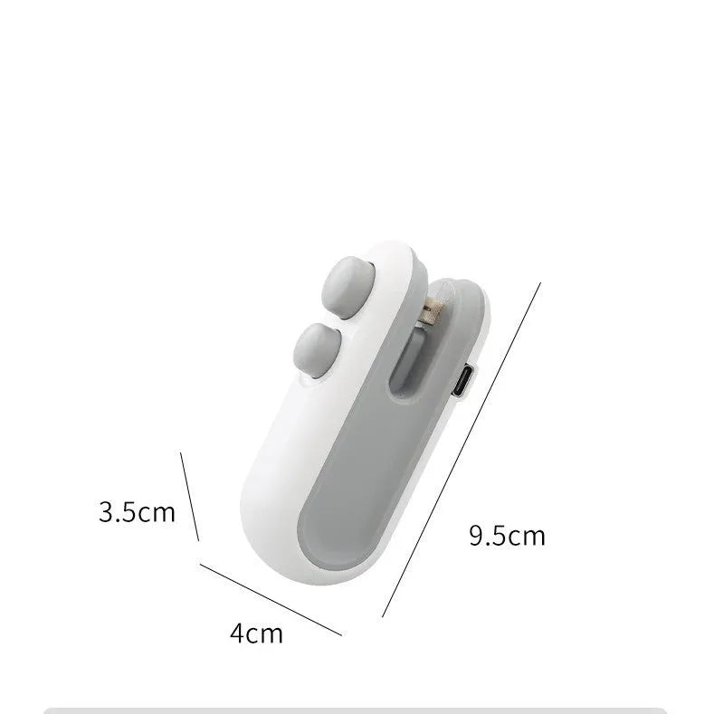White handheld vacuum sealing machine with USB port and cutter blade on a kitchen counter.